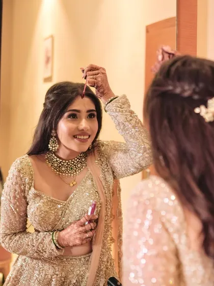 A final touch-up in the mirror. Her soft glam makeup and sparkling lehenga are ready for the party.