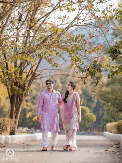 A cheerful walk down a tree-lined path. The couple's vibrant, color-coordinated outfits for their Haldi or Mehndi ceremony bring a splash of joy to this beautiful natural setting.