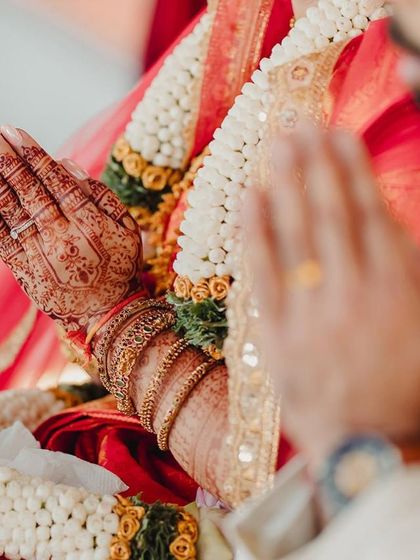 A close-up of the bride's hands during a wedding ceremony. The rich stain of the mehndi is clearly visible, adding to the auspiciousness of the moment.