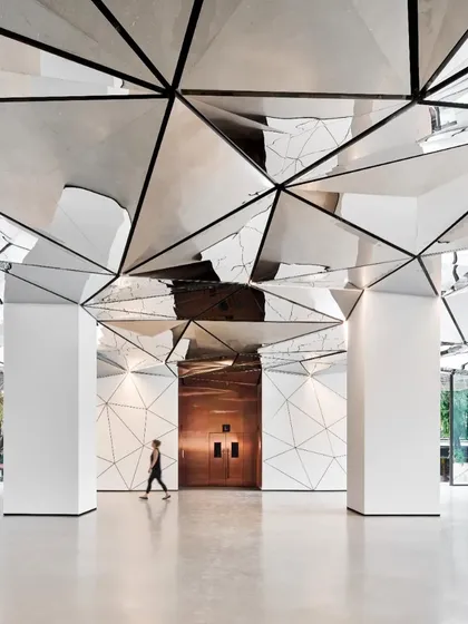 The lobby's depth is accentuated by the continuous geometric pattern on the walls and ceiling, leading the eye towards the warm, metallic tones of the elevator doors.