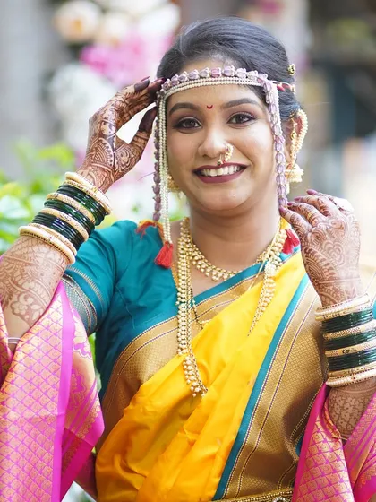 The bride adjusting her mundavalya, a classic Maharashtrian bridal pose. This shot highlights the traditional accessories and the flawless makeup application.