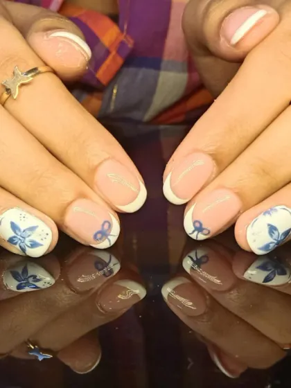 A beautiful French manicure featuring delicate blue floral and bow designs on the accent nails for a charming look.