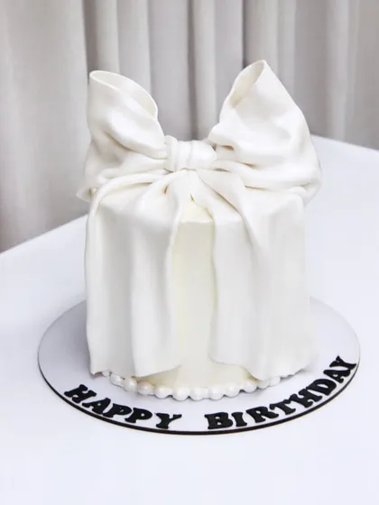 A simple and elegant birthday cake featuring a large, dramatic white bow made from fondant.