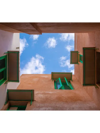A view looking up from another courtyard, this one with earthy-toned walls and bright green window frames. The use of color and texture helps define different spaces and creates a visually rich environment.