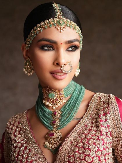 A close-up of a regal bridal look. The makeup features a sharp winged liner and a soft, neutral palette, allowing the intricate matha patti and multi-layered necklace to shine.