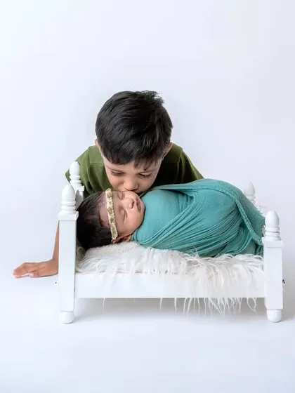 The beginning of a lifelong bond. An older brother gently kisses his newborn sibling, who is swaddled and resting in a miniature white bed. Sibling photos are a special part of my newborn sessions.