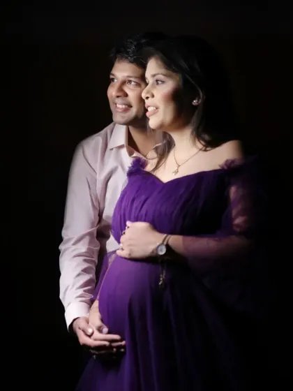 A classic low-key studio maternity portrait. The dramatic lighting highlights the couple's connection and the beautiful silhouette of the baby bump.