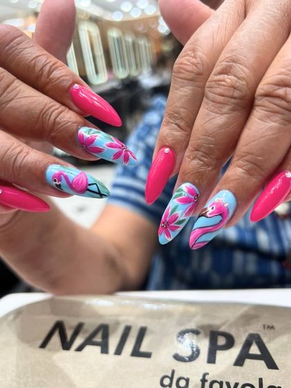 Stand out with this vibrant, tropical-themed nail art. The design features bright pink nails paired with accent nails showcasing hand-painted flamingos and floral patterns on a sky-blue background.