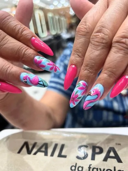 Stand out with this vibrant, tropical-themed nail art. The design features bright pink nails paired with accent nails showcasing hand-painted flamingos and floral patterns on a sky-blue background.