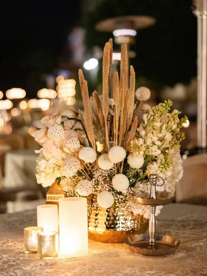 A textured centerpiece combining dried pampas grass, white billy balls, and hydrangeas in a hammered gold vase.