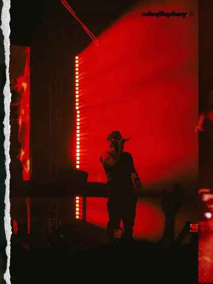 A wide shot of Talwiinder on stage, silhouetted against a massive red-lit screen. This image emphasizes the scale of the production and his solitary presence.