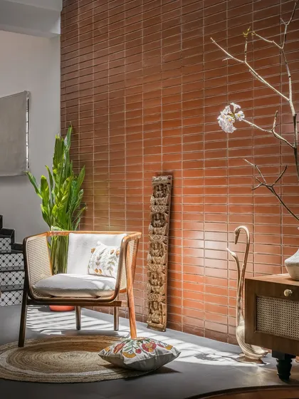 A quiet corner in the 'Ittige' residence highlights our focus on texture and materiality. The warmth of the terracotta brick wall contrasts with the smooth finish of the floor, while the custom cane chair and antique wooden carving add layers of craftsmanship and heritage to the minimalist space.