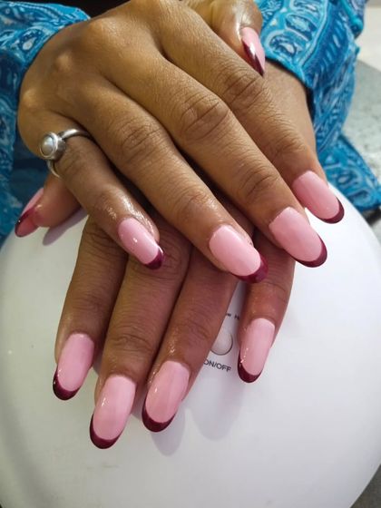 A modern take on the French manicure with bold, deep red tips on rounded gel extensions. The contrast between the pink base and the dark tips creates a very chic and sophisticated look.