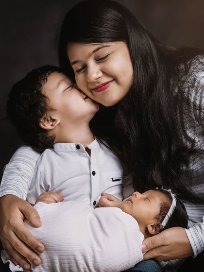A mother's embrace, holding her newborn while her son gives her a sweet kiss on the cheek. This is a classic, heartfelt family portrait that you will cherish forever.