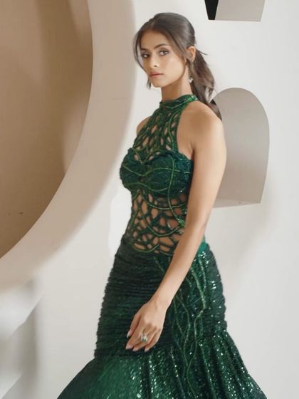 A closer look at the emerald green gown, focusing on the intricate cutwork on the bodice and the shimmering, embellished skirt.