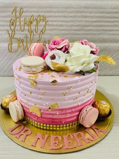 An elegant pink ombre cake for a doctor, decorated with gold leaf, macarons, and a mix of pink and white flowers.