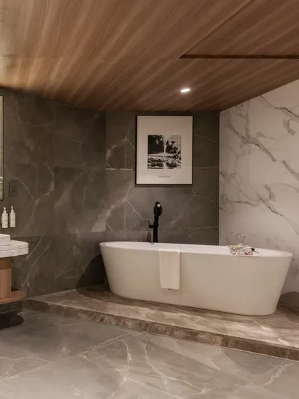 A spacious and luxurious bathroom suite at the Radisson Resort in Khopoli. The design features a freestanding oval bathtub set on a raised platform, contrasting grey and white marble walls, and a warm wood-paneled ceiling, creating a spa-like sanctuary for guests.