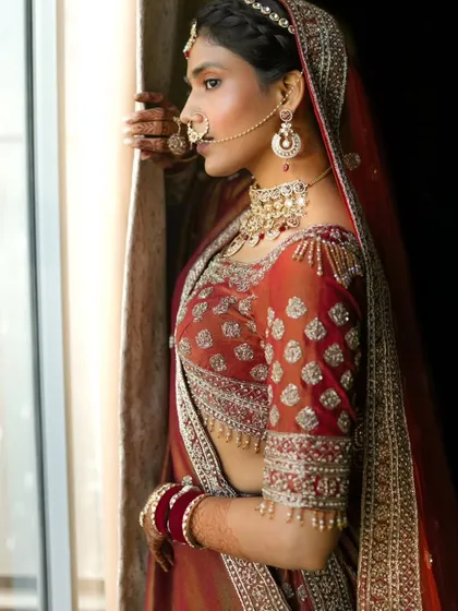 A classic bridal portrait by a window. The natural light beautifully illuminates her features, her traditional nath, and the detailed embroidery of her attire.