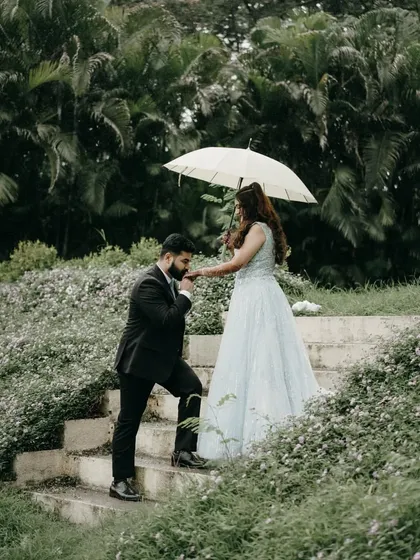 Creating a fairytale moment during a pre-wedding shoot. This shot, set against a lush green backdrop, uses a simple prop like an umbrella to create a scene filled with romance and classic charm, like a still from your own love story.