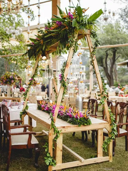 A unique dining table setup with a wooden A-frame structure overhead, adorned with tropical flowers and greenery. This created an intimate and beautifully framed dining experience for the head table.