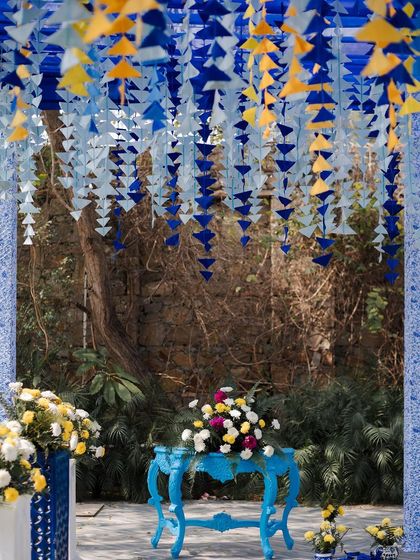 A beautiful composition of color and texture, with a blue vintage table set against a backdrop of hanging paper tassels and lush greenery.