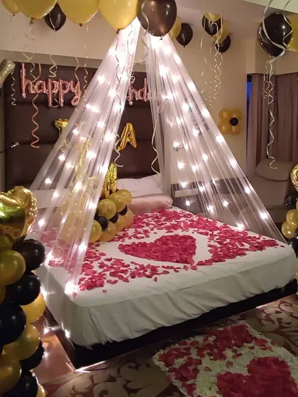 A closer look at a black and gold themed birthday decoration. This view highlights the heart-shaped rose petal arrangement on the bed and the combination of foil and latex balloons.
