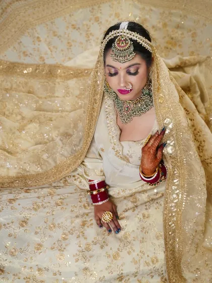 An ethereal bridal look in an ivory and gold lehenga. The student has created a soft, glowing look with a pop of color on the lips.