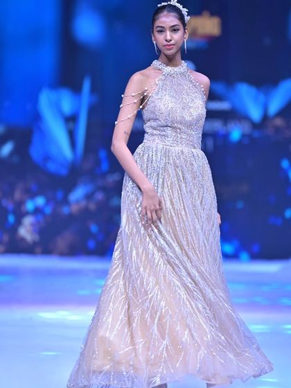 This halter-neck gown is crafted with shimmering silver fabric that drapes beautifully, creating a look of effortless glamour.