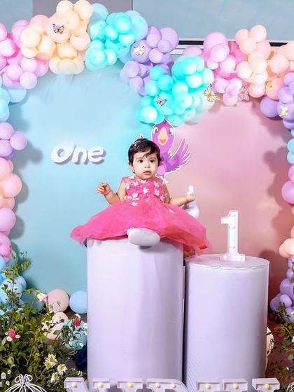 The birthday girl sits proudly on her throne at her whimsical first birthday party. The pastel-colored balloon arch and cute animal cutouts create a soft and dreamy setting for her special day.