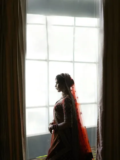 A powerful silhouette of the bride against a bright window. This artistic shot creates a sense of anticipation and highlights her beautiful form.