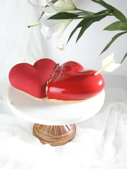 A modern and artistic Valentine's cake. This heart-shaped entremet features two textures, velvet and mirror glaze, and is pierced by Cupid's arrow.
