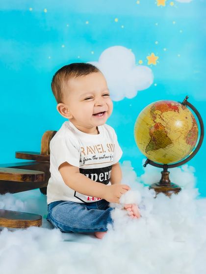 A moment of pure laughter from a baby boy during his aviator-themed photoshoot, surrounded by clouds and a toy plane.