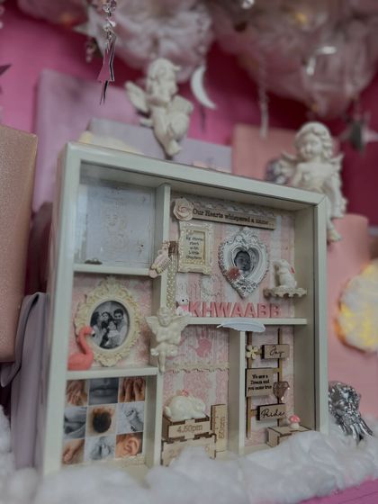 A detailed shot of the custom shadow box, featuring photos, the baby's name, and other precious keepsakes in a beautiful arrangement.