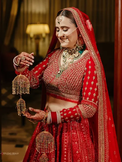 A radiant bride in her red lehenga, smiling as she holds her 'kalire', captured in a moment of happy anticipation.
