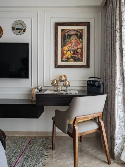 A compact and functional study nook carved out in a bedroom. The floating desk and classic chair are placed beside the TV unit, with traditional Indian art adding a touch of cultural elegance.