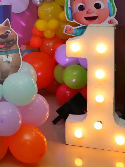 A light-up marquee number '1' next to a Cocomelon character cutout. This is a great way to highlight a first birthday while sticking to the party's theme.