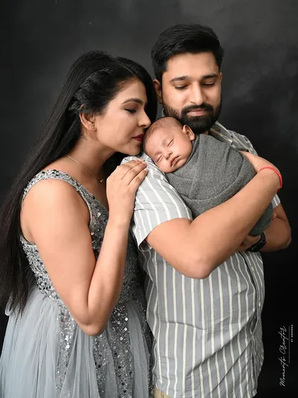 A peaceful moment between new parents and their baby. The mother leans her head on the father's shoulder as he holds their sleeping newborn, a picture of pure serenity.