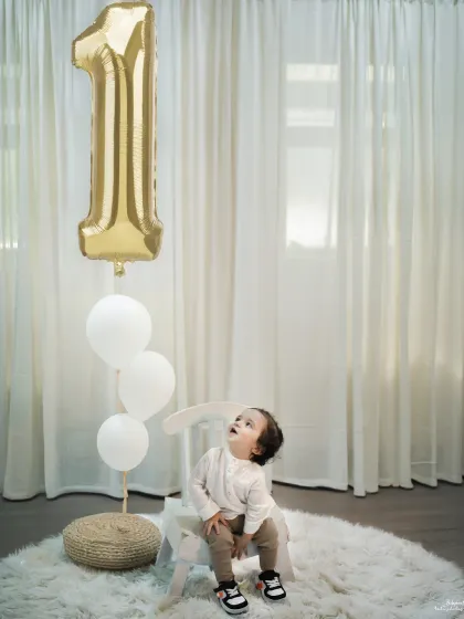 Looking up in wonder at the number '1' balloon. This is a classic and timeless first birthday portrait that captures the magic of this special milestone.