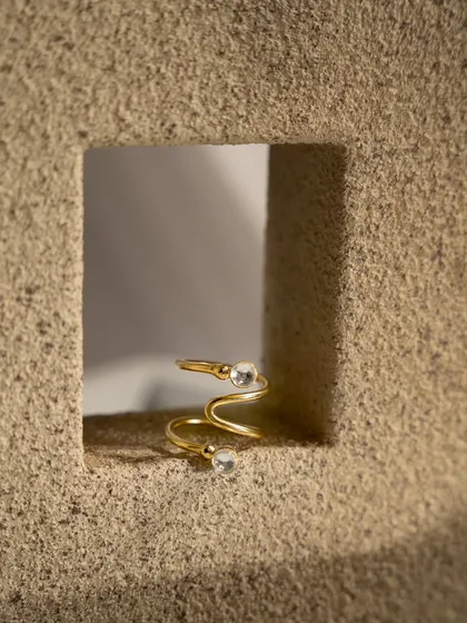 A detailed macro shot of a gold spiral ring. The tight framing and textured background highlight the unique design and craftsmanship of the piece, perfect for a product page.