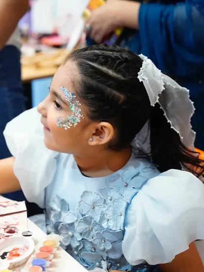A young guest with beautiful glitter face paint gets creative at the art station during a 'Frozen' party.