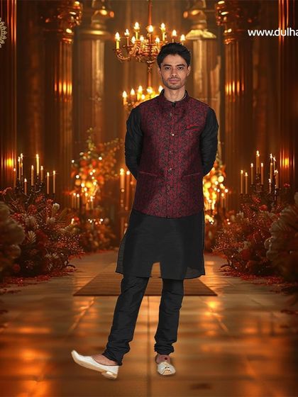 A black kurta paired with a red and black patterned Nehru jacket, set against a festive, candle-lit background.