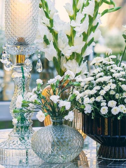 A close-up of the elegant tablescape, featuring white gladioli and chrysanthemums. The cut-glass candle holders and vases catch the light, complementing the shimmering Thikri decor throughout the venue.