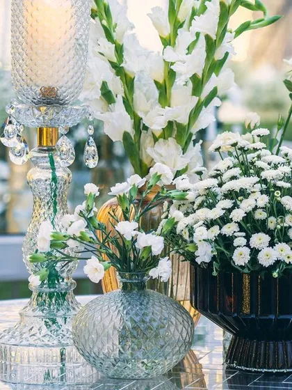 A close-up of the elegant tablescape, featuring white gladioli and chrysanthemums. The cut-glass candle holders and vases catch the light, complementing the shimmering Thikri decor throughout the venue.