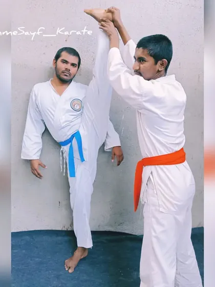 Karatekas in action. One student practices a high kick with assistance, a great way to improve flexibility and kicking technique.