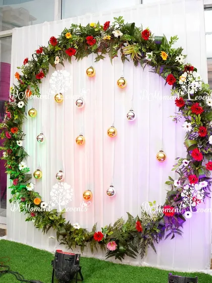 A beautiful floral photo booth for the anniversary party. A large ring made of fresh flowers and greenery, with hanging gold and silver ornaments, provides a perfect spot for guest photos.
