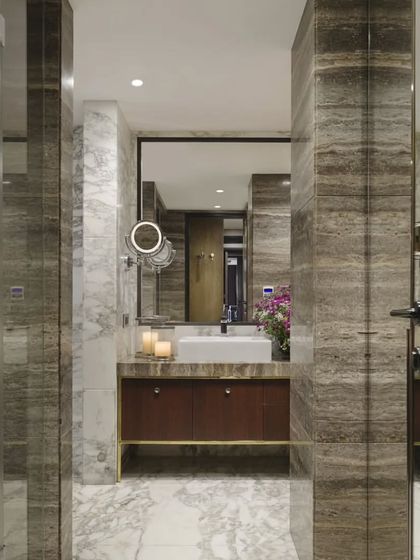 The master bathroom in the Caitriona apartment is a study in architectural elegance. Arbascato and Ebony travertine marble clad the walls and floors, while the custom vanity features an Aukupira veneer front and a brass base, creating a rich and luxurious palette.