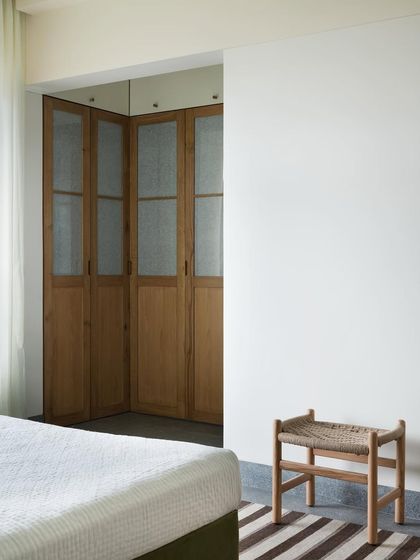 A minimalist stool with a handwoven seat, placed at the foot of the bed. I design small, versatile pieces like this to add texture and utility, providing a simple spot to rest or place things.