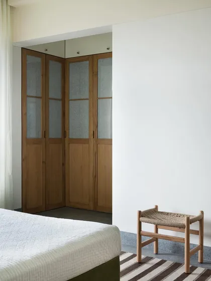 A minimalist stool with a handwoven seat, placed at the foot of the bed. I design small, versatile pieces like this to add texture and utility, providing a simple spot to rest or place things.