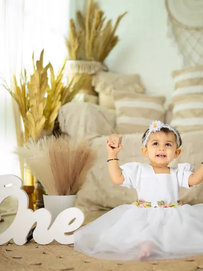 A little princess celebrating her first birthday. The simple white dress and clean, bright background create a timeless and elegant portrait.