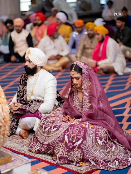 The bride and groom seated before the Guru Granth Sahib during their Anand Karaj. This wide shot captures the solemnity and beauty of the sacred ceremony.